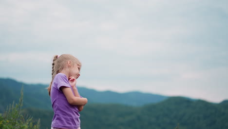 Coquettish-child-touches-cheek-by-finger-against-mountains