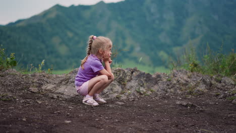 Tired-girl-sits-on-haunches-leaning-on-palm-on-rocky-hill