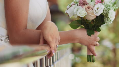 Bride-with-fresh-roses-bouquet-leans-on-balcony-railing