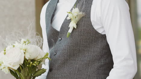 Elegant-young-man-in-grey-vest-with-boutonniere-and-flowers
