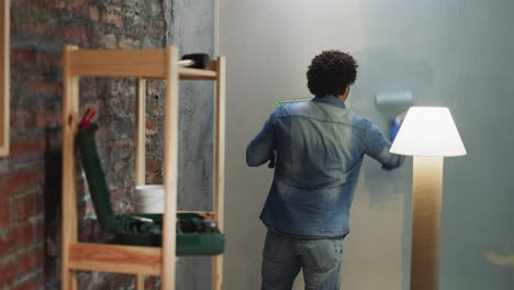 Black-man-in-denim-shirt-and-jeans-paints-wall-in-room