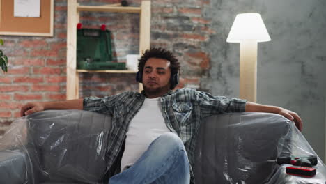 Black-man-with-headphones-nods-head-to-music-on-foiled-sofa