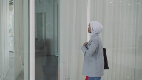 African-American-woman-adjusts-hijab-near-glass-wall