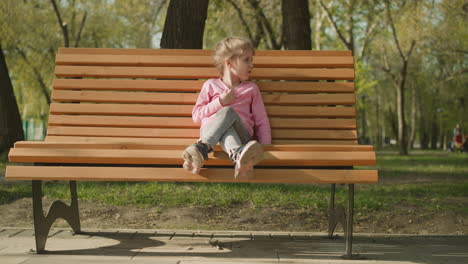 Little-girl-suffers-from-hot-weather-sitting-on-park-bench