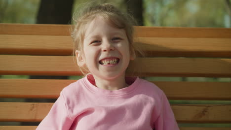 Joyful-girl-without-tooth-sits-on-bench-in-spring-park