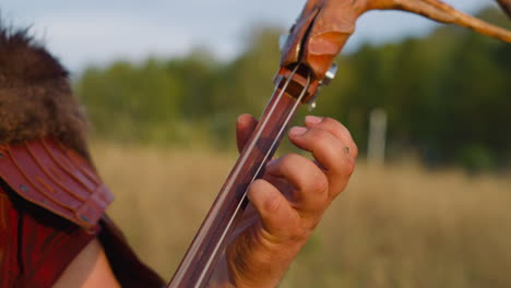 Folk-musician-presses-strings-on-deck-playing-ikili-on-field