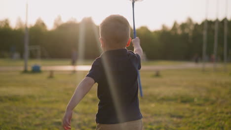 Cute-little-boy-runs-raising-up-scoop-net-along-playground