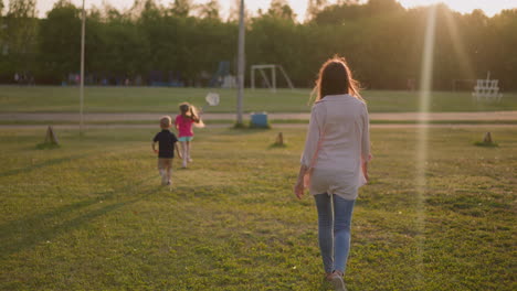 Woman-with-little-children-walks-to-sports-ground-at-sunset