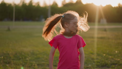 Happy-little-girl-shakes-long-ponytails-on-stadium-field