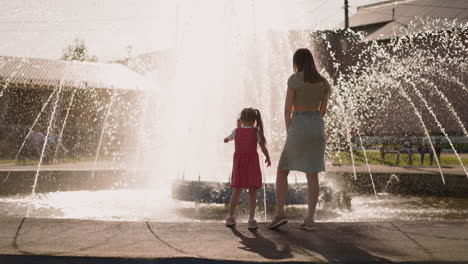 Girl-touches-fountain-water-and-takes-mother-hand-in-park