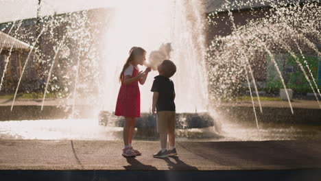 Little-boy-and-girl-bite-candy-floss-standing-by-fountain