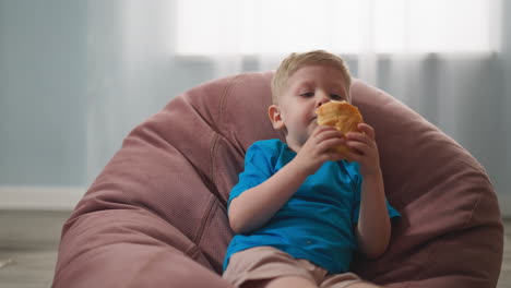 Toddler-boy-eats-puff-pie-sitting-in-bean-chair-at-home