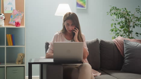Woman-with-laptop-talks-via-phone-near-daughter-on-sofa