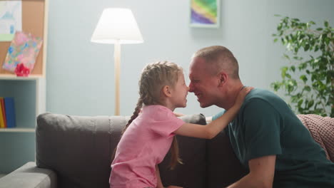 Joyful-father-and-little-daughter-touch-noses-in-living-room