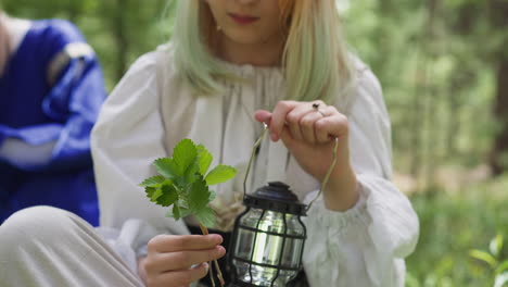 Teenage-girl-in-vintage-dress-looks-at-leaves-holding-lamp