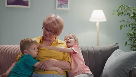 Adorable-little-children-hug-grandmother-in-living-room