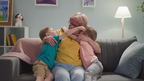 Happy-children-kiss-and-embrace-grandmother-in-living-room