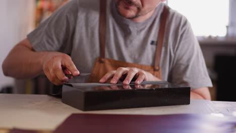 Craftsman-sharpens-cutter-with-sandpaper-at-table-in-shop