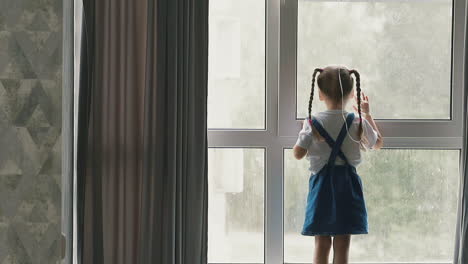 little-girl-stands-near-window-staring