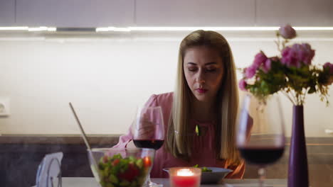 Pretty-woman-with-red-wine-eats-juicy-salad-at-table