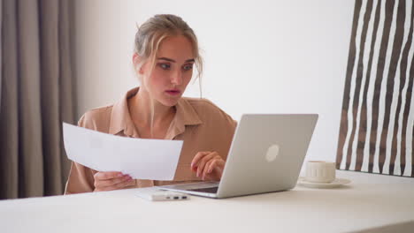 Young-woman-does-paper-work-looking-at-screen-of-laptop