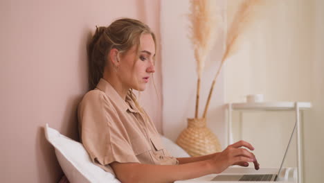Young-freelancer-woman-works-on-laptop-in-bed-at-home