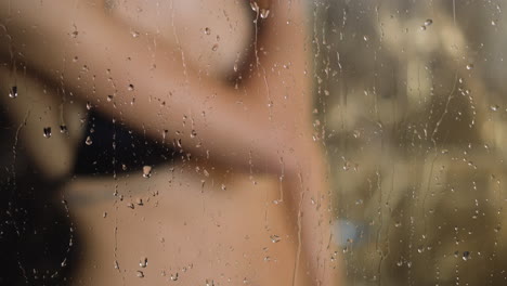 Woman-takes-shower-behind-transparent-cabin-misted-glass