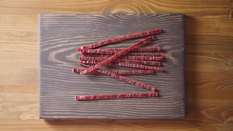 Person-drops-jerked-fish-sticks-onto-wooden-countertop