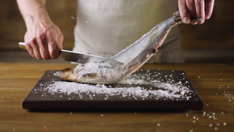 Chef-removes-salt-from-herring-fish-with-knife-on-board