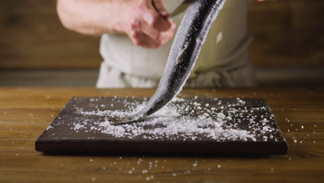 Man-uses-knife-to-clean-herring-from-salt-on-wooden-board
