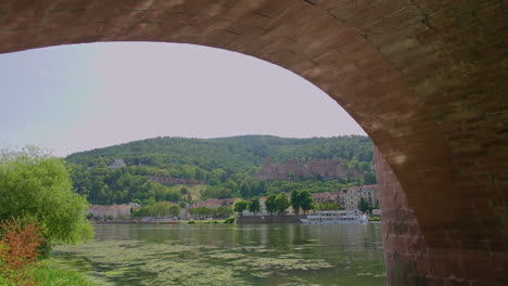 Heidelberg-view-under-Karl-Theodor-Brücke-bridge,-river-neckar,-a-tourist-boat-on-a-sunny-day