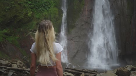 Attractive-blond-woman-watching-powerful-water-flow-of-waterfall-in-canyon