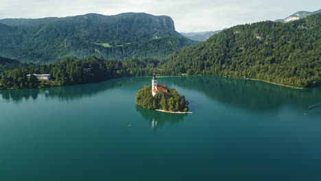 Bled-Island-Slovenia-in-calm-empty-lake-reflecting-sky,-aerial-orbit