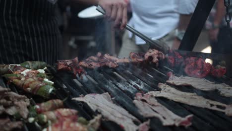 Slow-motion-shot-of-a-street-vendor-flipping-meats-on-hsi-grill-with-metal-tongs