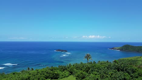 green-mountainside-to-reveal-tropical-ocean-breaks-and-blue-sky,-drone