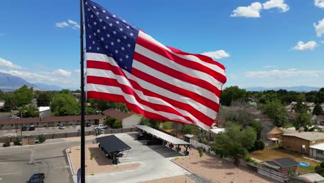American-flag-USA-blowing-waving-in-the-wind-on-beautiful-sunny-summer-day-with-clouds-and-blue-skies-overlooking-mountains-drone-slowly-panning-clockwise-around-flagpole---in-4K-60fps