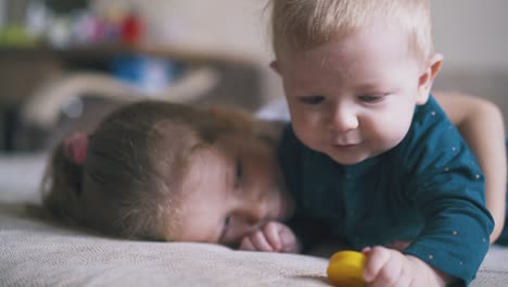 Kleines-Mädchen-Umarmt-Seinen-Süßen-Bruder,-Der-An-Einem-Gelben-Spielzeug-Auf-Dem-Bett-Knabbert