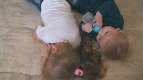 adorable-baby-drinks-water-and-elder-sister-lies-on-bed