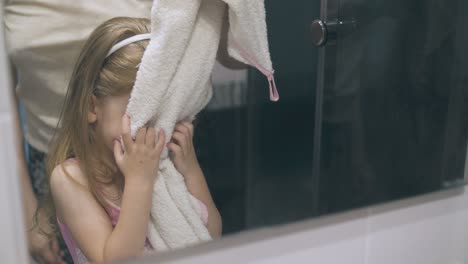 cute-girl-wipes-face-by-mother-holding-towel-at-mirror