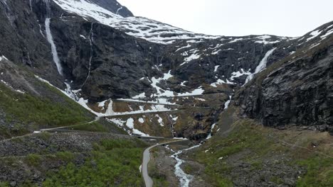 Trollstigen-mountain-pass-days-before-opening-with-snow-left-in-terrain---Aerial-approaching-hillside-above-closed-road