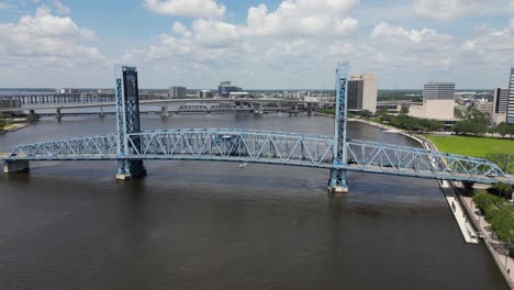 boat-cruising-under-main-street,-John-T-Alsop,-bridge-in-Jacksonville-Florida-viewed-from-off-center-stationary-drone