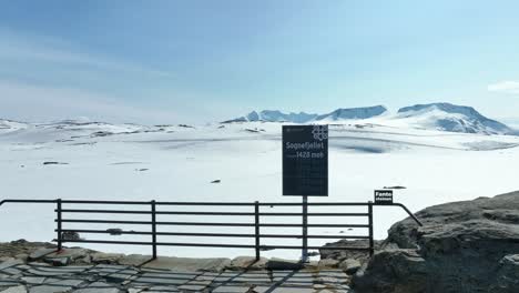 Sign-on-top-of-Sognefjellet-mountain-pass-informing-about-altitude-1428-meters-above-sea-level---Snowy-background-during-summer