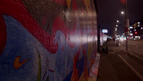 Close-up-of-colorful-Berlin-wall-graffiti-at-night-with-city-lights-reflection