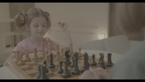Grandmother-teaching-to-play-chess-her-small-granddaughter-at-home