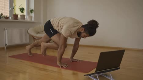 Fit-mixed-race-athletic-man-watching-online-training-classes-on-laptop,-repeating-moves-after-instructor