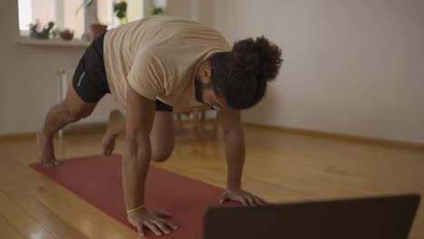 Young-male-working-out-at-home-in-his-living-room,-doing-push-ups-with-legs-lunges-on-a-yoga-mat