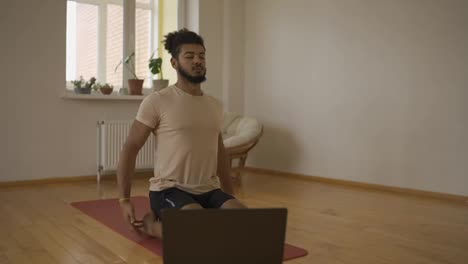 Bearded-sporty-male-breathing-deeply,-sitting-with-closed-eyes-on-exercise-mat-in-living-room