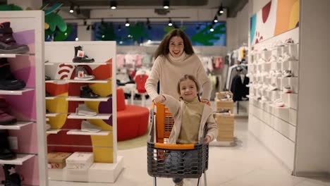 Lustige-Aktion-Von-Mutter-Und-Kind,-Die-Mit-Einem-Einkaufswagen-In-Ein-Modernes-Handels--Oder-Einkaufszentrum-Gehen