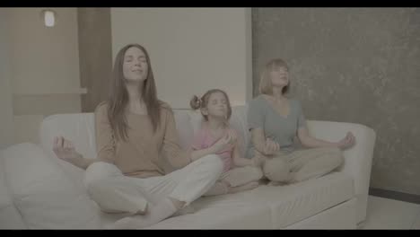 Dos-Mujeres-Maduras-Y-Una-Niña-Están-Sentadas-En-El-Sofá-En-Una-Pose-De-Yoga-Y-Meditando
