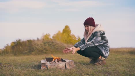 woman-hiker-heats-hands-at-bonfire-in-camp-in-autumn